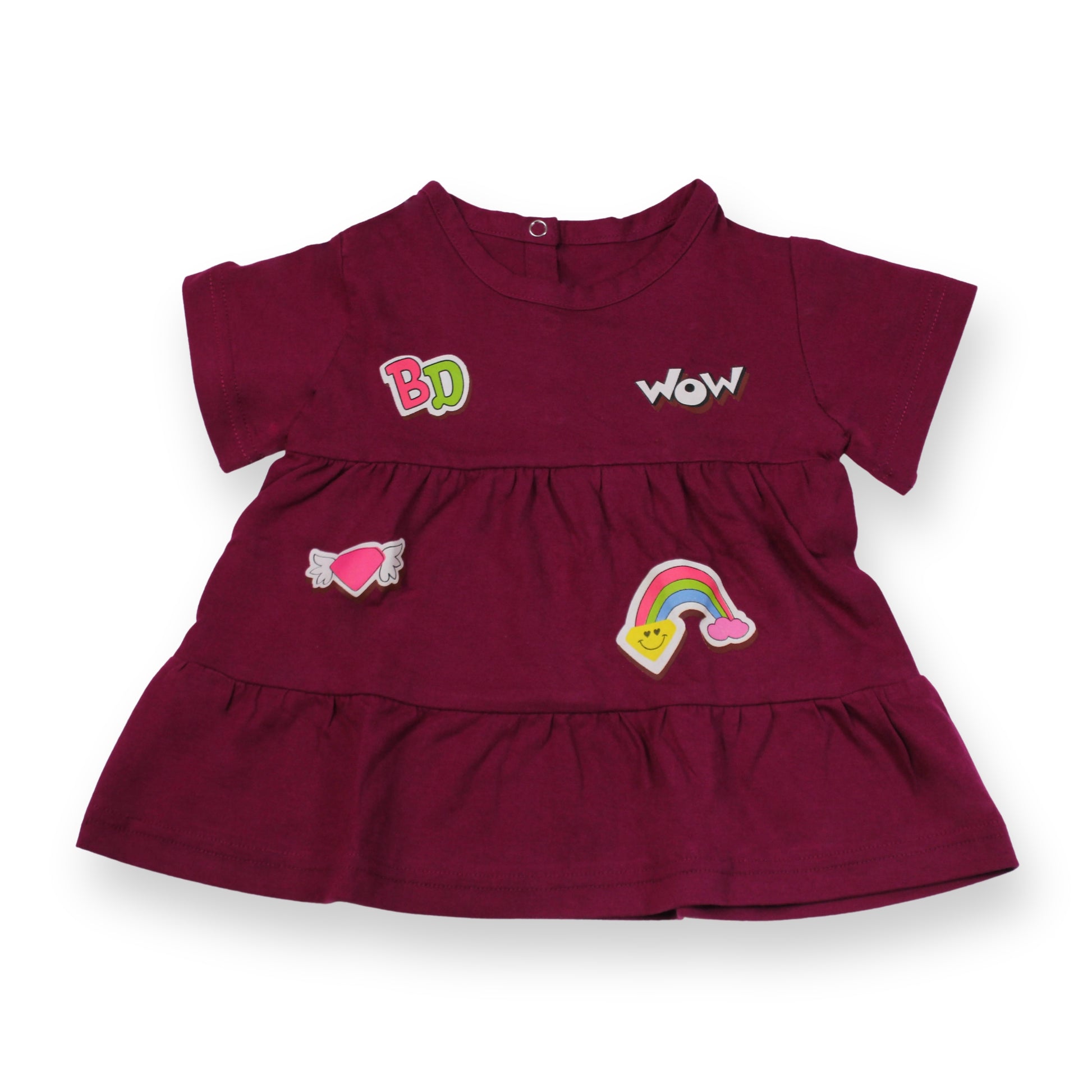 A Babydrip magenta short-sleeve tunic blouse with ruffled tiers, featuring embroidered patches including 'BabyDrip', (BD) 'WOW', a pink heart with angel wings, and a rainbow on a white background. Laid out flat on a white background.