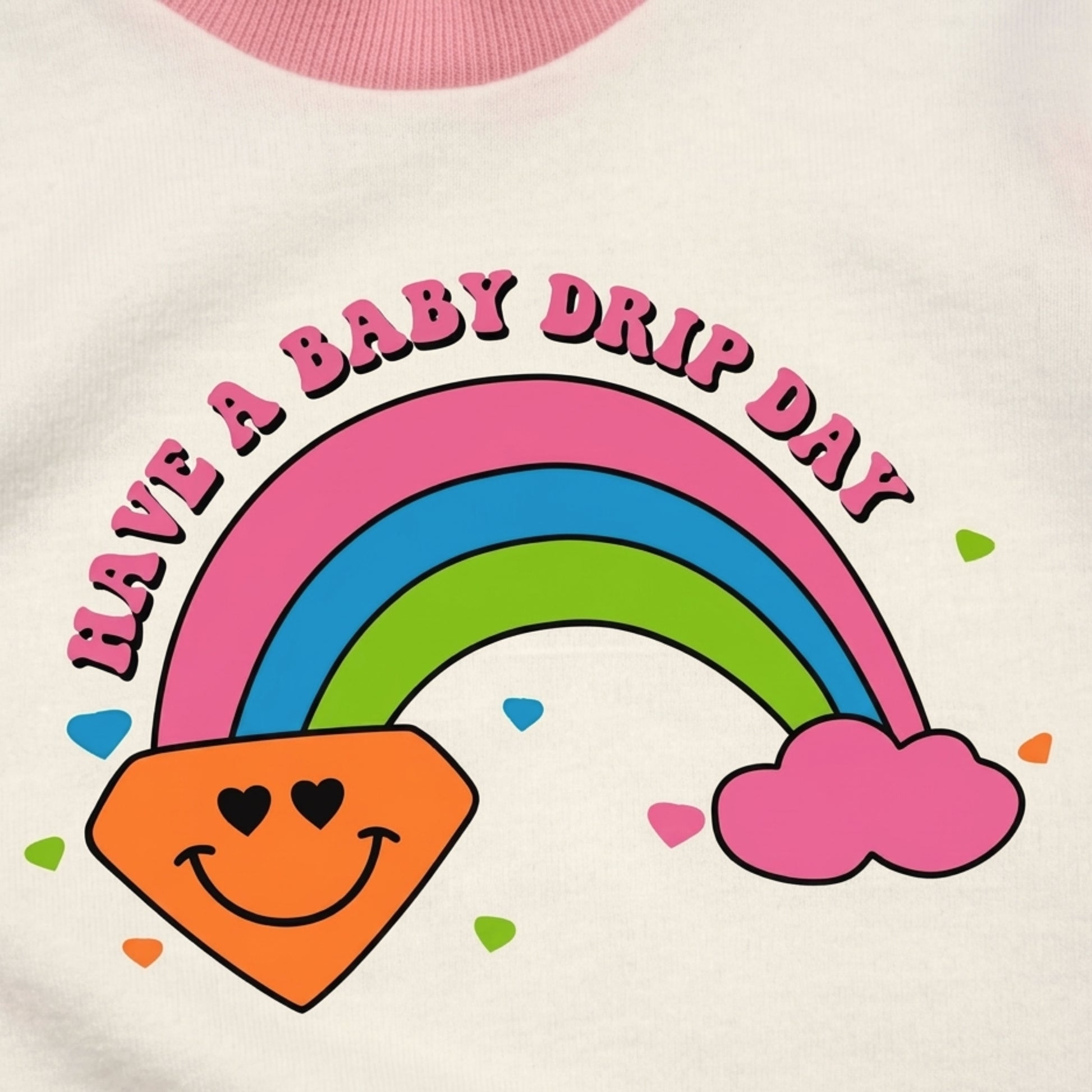 Close-up of a white Babydrip garment with a colorful printed graphic reading 'HAVE A BABY DRIP DAY' above a colorful rainbow, pink cloud, and smiling orange diamond shape with colorful small diamonds surrounding the lower section of the rainbow.