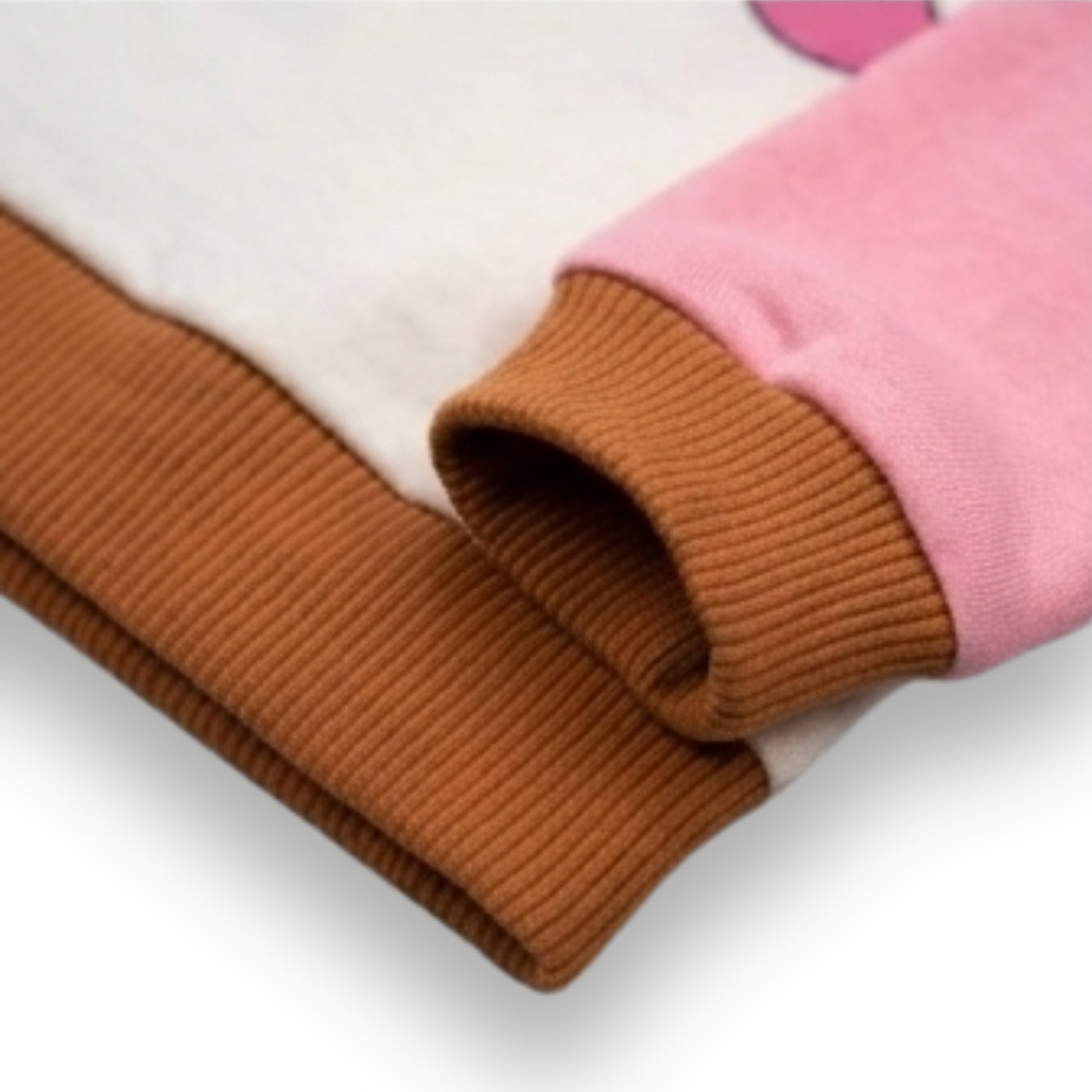 Close-up of a Babydrip folded girl's sweatshirt showing a white body, a pink sleeve, with a ribbed brown cuff and hem on a white background.
