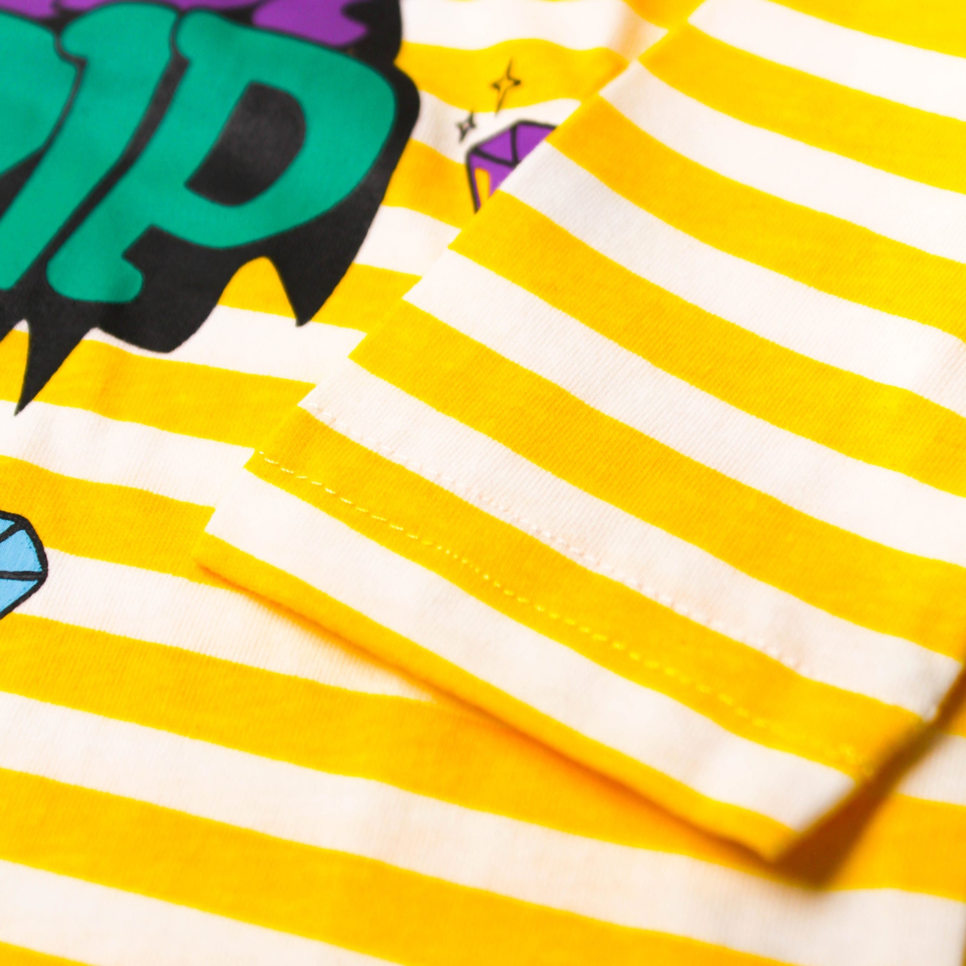 Close-up image of babydrip yellow and white striped garment with a colorful graphic print partly showing and folded fabric detail.