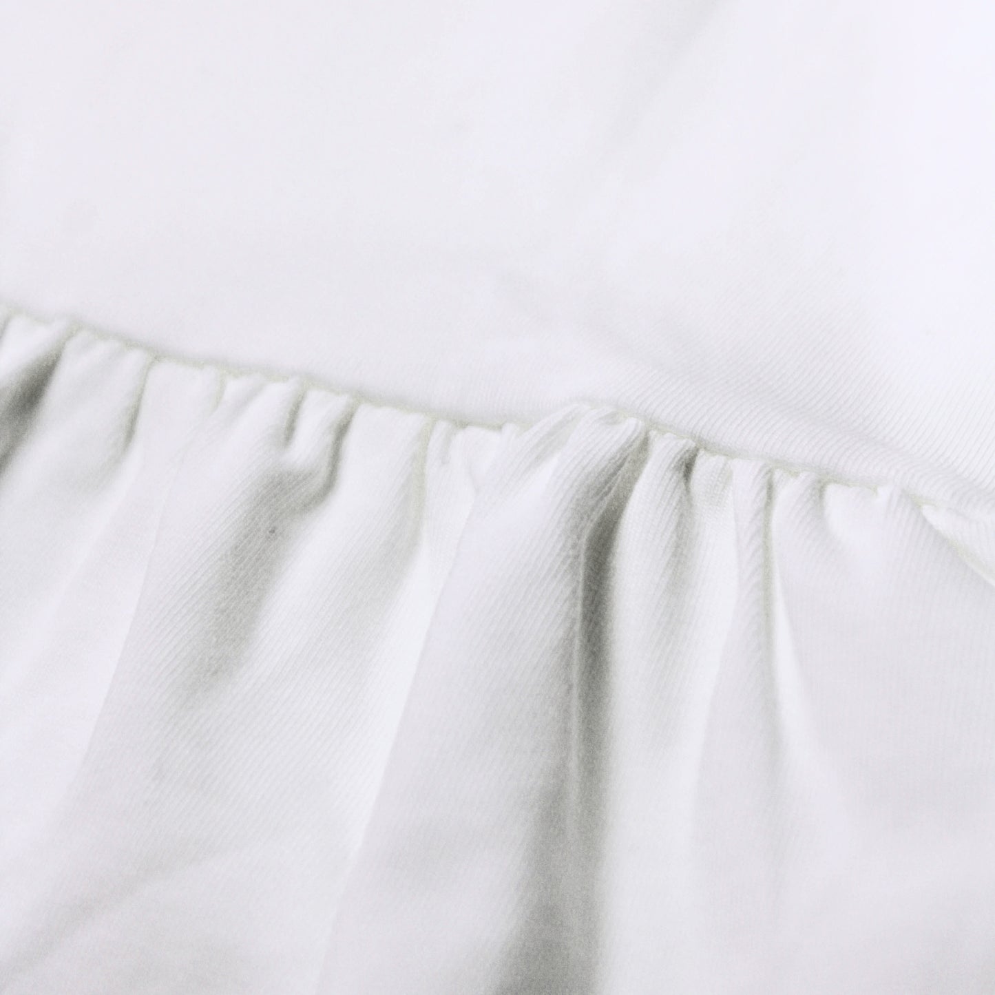Close-up image of a white fabric product showing a gathered ruffle seam and soft texture from babydrip collection.