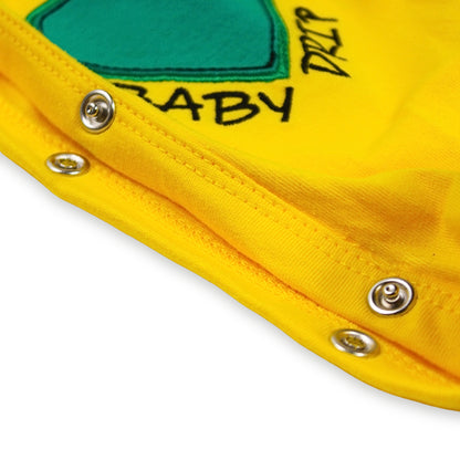 Close-up image of a bright yellow garment with metal snap button closures along the inside seam, with a green embroidered patch, and partial black text reading 'BABY DRIP'. On a white background.