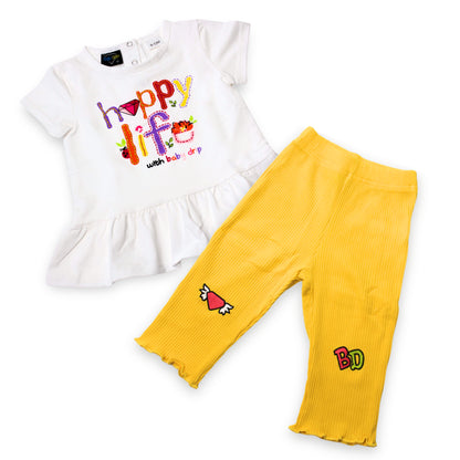 Babydrip girls 2-piece outfit featuring a white short-sleeve peplum top with a colorful 'Happy Life' graphic and yellow ribbed leggings with embroidered patches on a white background.