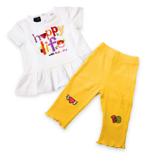 Babydrip girls 2-piece outfit featuring a white short-sleeve peplum top with a colorful 'Happy Life' graphic and yellow ribbed leggings with embroidered patches on a white background.