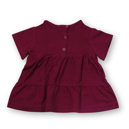A Babydrip short-sleeve Magenta tunic blouse with a tiered ruffle hem and three snap open and shut silver buttons on the back neckline, shown laid flat against a plain white background.