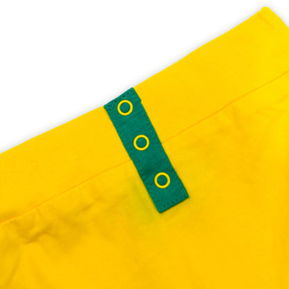 A close-up image of a bright yellow Babydrip garment waist with a green fabric tab featuring three yellow grommets, set against a plain white background.